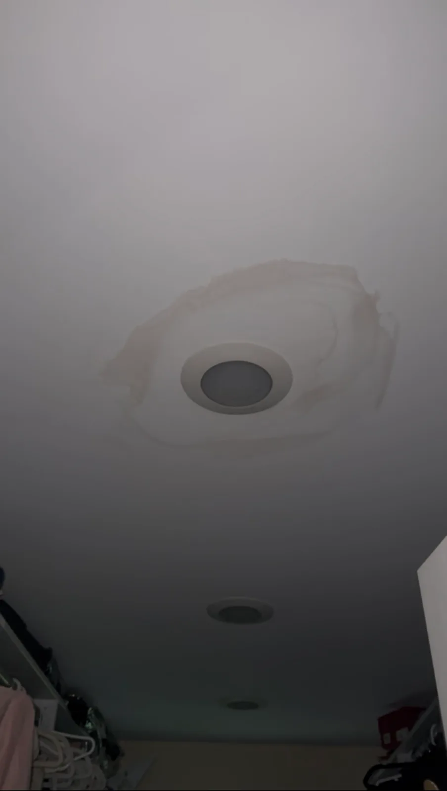 A white ceiling in a closet with a recessed light fixture surrounded by a freshly painted repair patch.