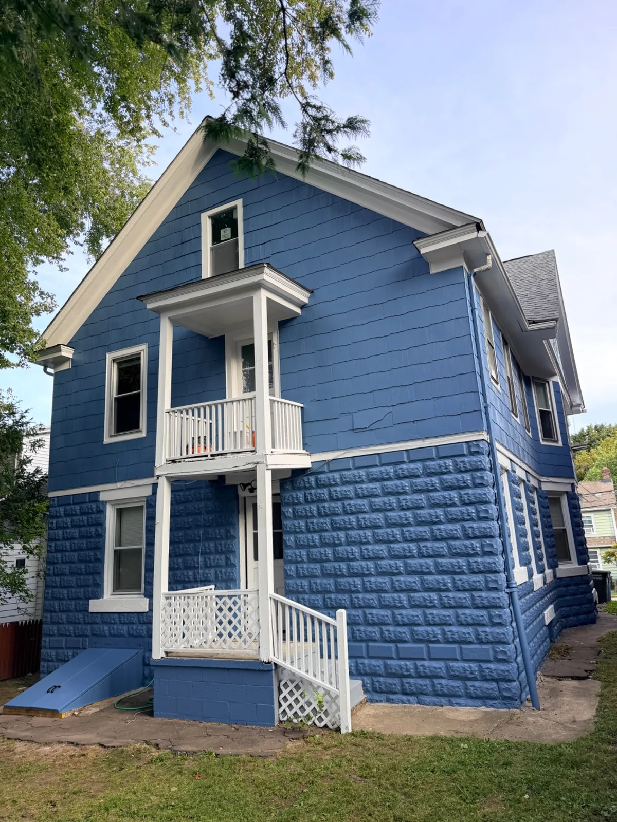 The exterior of a blue house in Bridgeport after a full paint job, including siding and stone foundation detail.
